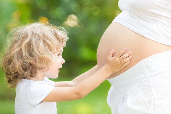 Ein Kind im Grundschulalter berührt den dicken Bauch der schwangeren Mutter.